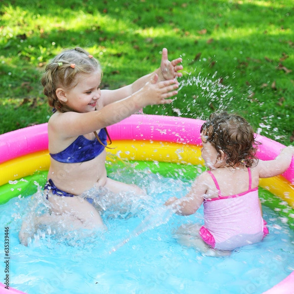 Fototapeta Children in the pool, it's hot in the summer. A little girl. A child plays in a children's pool. Swimming in the yard, inflatable pool in the shade. The girl loves water. Happy child in a swimsuit