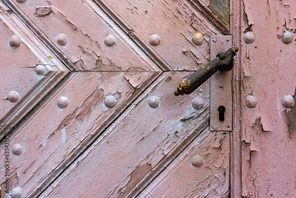 Fototapeta Close-up of an old, wooden door with a handle and keyhole. The door is made from planks of wood that have been weathered by the elements over time, giving it a rustic look.