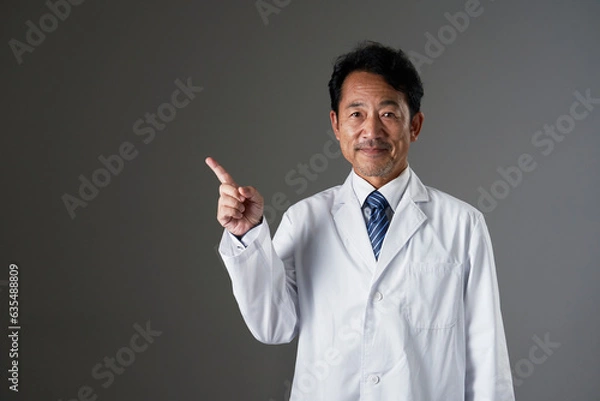 Fototapeta 左側を指差すミドルエイジの医者　黒背景