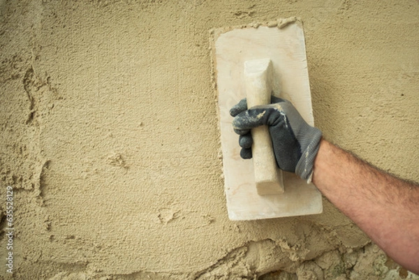 Obraz "A worker smoothes the material applied to a stone wall with a trowel."