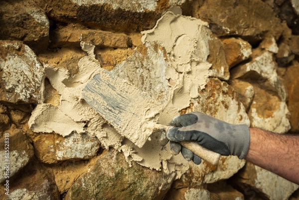 Obraz A laborer applies a product to a stone wall with a trowel to begin construction.