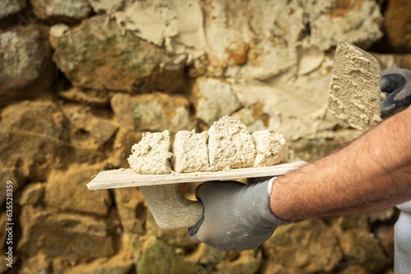Obraz A laborer applies a product to a stone wall with a trowel to begin construction.