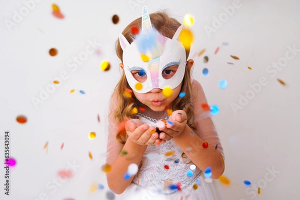 Fototapeta A child in a carnival mask of a unicorn, hand-made from glitter foamiran and faur fux. Little cute cheerful comical girl in the role of a unicorn, preparing for the carnival, masquerade, holidays.