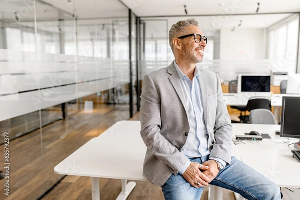 Fototapeta Serene modern middle aged businessman in formal wear leaned on the desk looking away, inspired and calm mature business owner at the office, confident grey-haired man in relaxed pose
