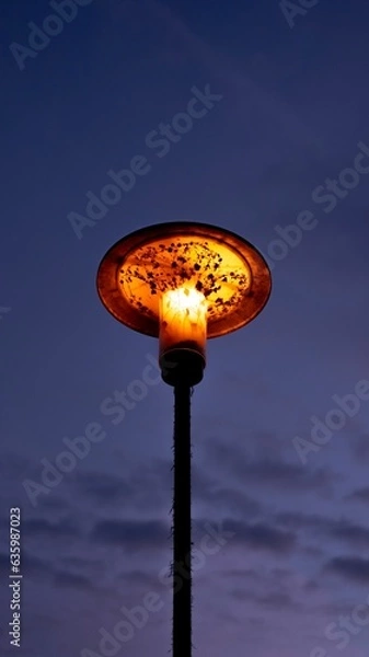 Fototapeta Vertical low angle shot of a glowing old street lamp under a blue sky