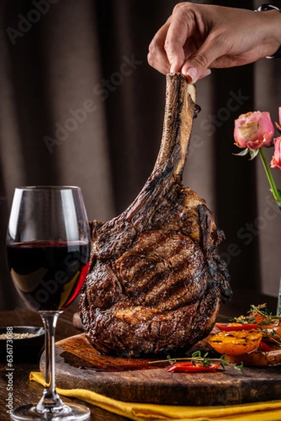 Obraz The chef holds a large piece of roasted meat on the bone, tomahawk, lamb or veal.
