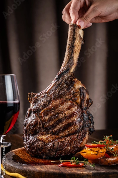 Obraz The chef holds a large piece of roasted meat on the bone, tomahawk, lamb or veal.