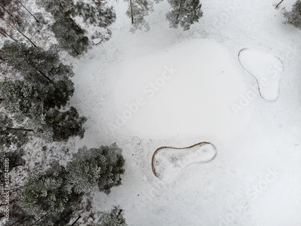 Obraz Aerial view of a golf cart with fairway, bunkers and putting green covered with snow. Photography taken from above with a drone in Sweden in winter. 