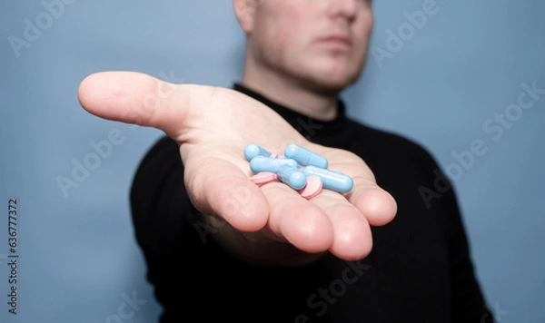 Obraz The concept of treatment with antibiotic pills. Medical capsules in a man's hand on a blue background. Medical preparation in tablets. drugs