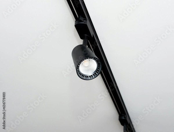 Obraz Background Led track lamp on the ceiling in the interior. Interior spotlight in black color. Modern track lamp with a lot of swivel lamps. The concept of lighting in the house.