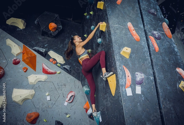 Fototapeta A strong female climber climbs an artificial wall with colorful grips and ropes.