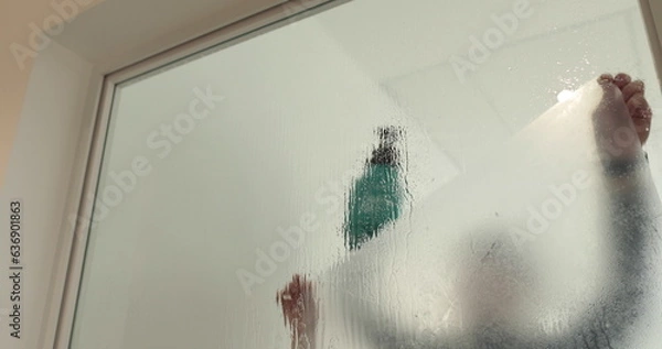 Fototapeta A man pastes a frosted coating on a glass door in a clinic to make the glass door opaque. Applying a matte coating to the glass.