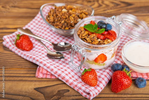 Fototapeta Bowl of granola with yogurt and fresh berries on a texture table. Yogurt berries, acai bowl, spirulina bowl. Healthy food, balanced breakfast. Strawberries, blueberries, kiwi, peach, almonds and chia.