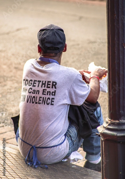 Fototapeta Restaurant employee with his back to camera, wearing "end gun violence" tee shirt while eating during a break