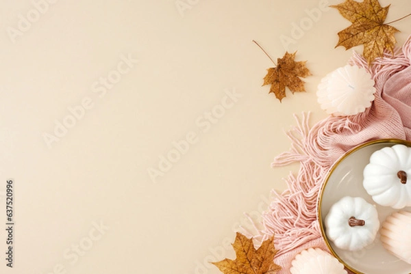 Fototapeta Immerse yourself in the tranquil and snug comforts of fall at home. Top view photo of warm pink plaid, pumpkins, candles, autumn maple leaves on pastel beige background with empty space for ad or text