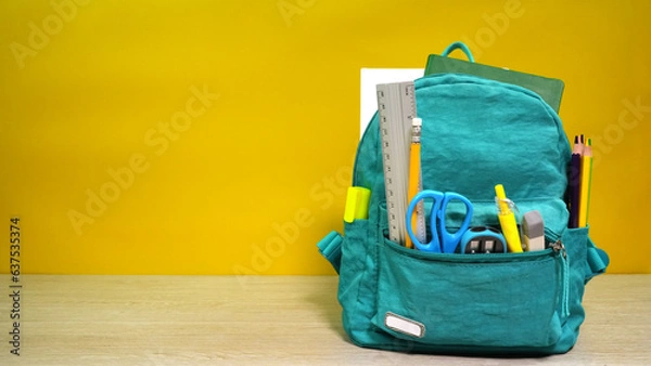 Fototapeta Turquoise backpack with different school stationery on yellow background. Space for text