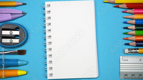 Fototapeta A schoolchild's workplace with an open notebook, pencils, pens, ruler and other stationery on blue background. Back to school concept. Top view. Copy space