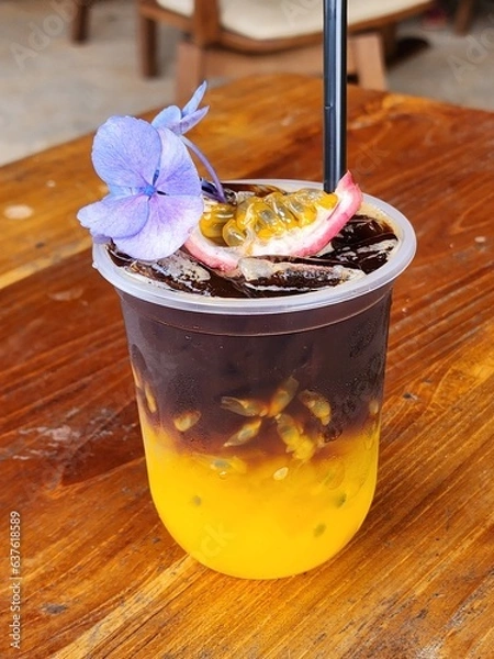 Fototapeta Ice americano with orange juice  and passion fruit  on top. Decorate ith  Flower .The cup put on the old wood table