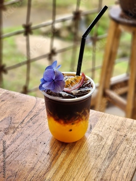Fototapeta Ice americano with orange juice  and passion fruit  on top. Decorate ith  Flower .The cup put on the old wood table