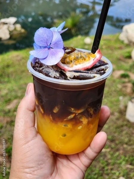 Fototapeta Ice americano with orange juice  and passion fruit  on top. Decorate ith  Flower .The cup put on the old wood table
