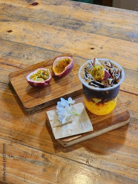 Fototapeta Ice americano with orange juice  and passion fruit  on top. Decorate ith  Flower .The cup put on the old wood table