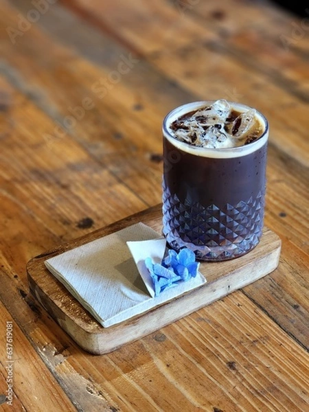 Fototapeta Iced americano coffee glass put on wood tray and put on old wood table. Decorate with flowers .wooden table and glass bottle and tissue paper