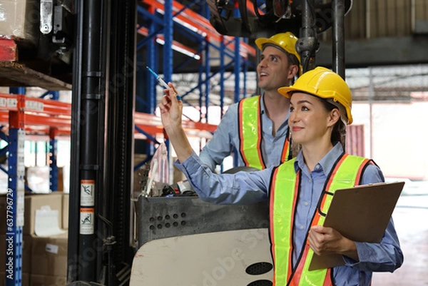 Fototapeta Group of warehouse workers with hardhats and reflective jackets using tablet, walkie talkie radio and cardboard while controlling stock and inventory in retail warehouse logistics, distribution center