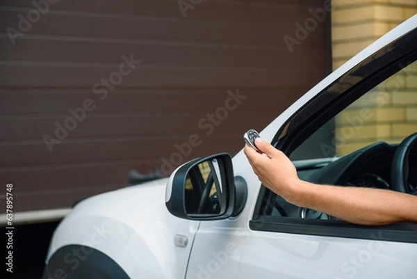 Obraz man's hand presses the remote to open the garage door