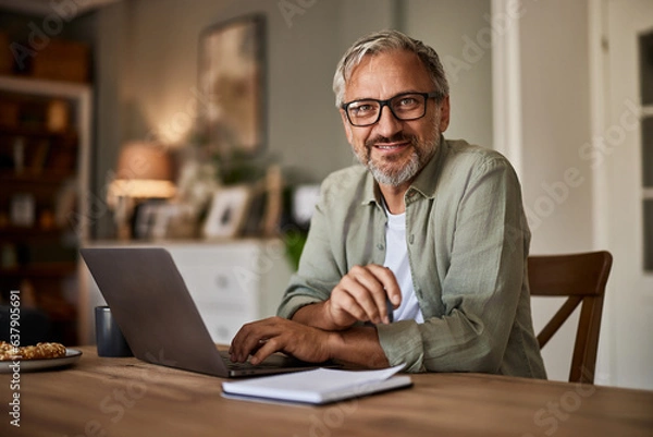 Fototapeta Portrait of a smiling male freelancer with glasses on working on a laptop.