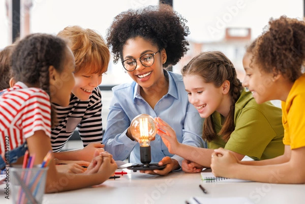 Fototapeta Multiethnic teacher and kids studying electricity and incandescent light bulb at physics lesson.