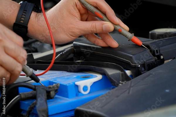Obraz technician checks the battery using a voltmeter capacity tester,auto mechanic uses a multimeter voltmeter to check the voltage level in a car battery