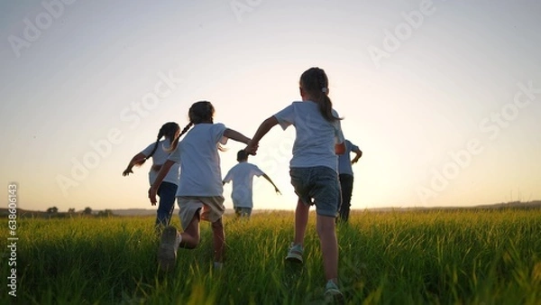 Fototapeta a group of children run across the field on the grass. happy family kid lifestyle dream concept. children running in a field with tall grass on the sunset. girls holding hands in the foreground
