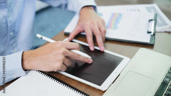 Fototapeta Businessman or manager taps tablet embracing the world of technology and internet focus on finance searching for information online from corporate matters to marketing strategies. In his modern office