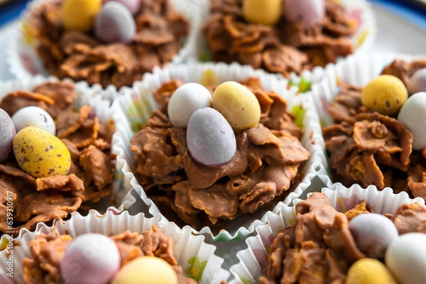 Fototapeta Chocolate pastries shaped like baskets with eggs, packaged in paper, rest on a plate