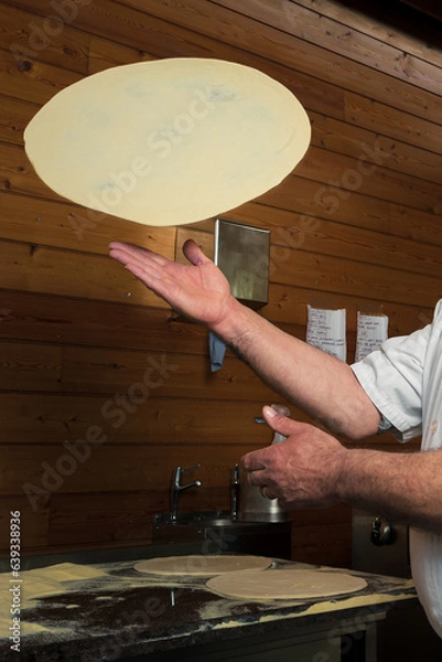 Obraz A skillful chef is preparing pizza, twirling the dough, making thin crust for delicious Italian pizza in an upscale restaurant