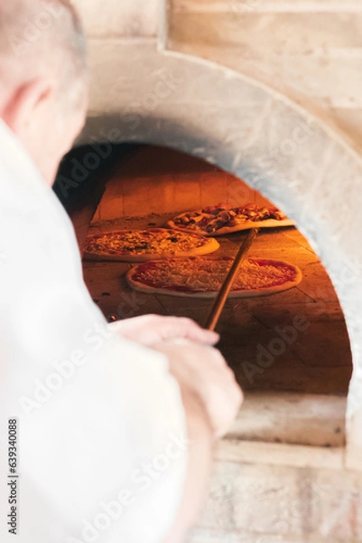 Obraz A talented French chef places a cheese and sausage pizza into the hot oven for 5 minutes