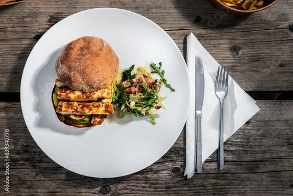 Obraz A burger and a salad on a white plate at an outdoor café on a wooden table, clean cutlery and napkin