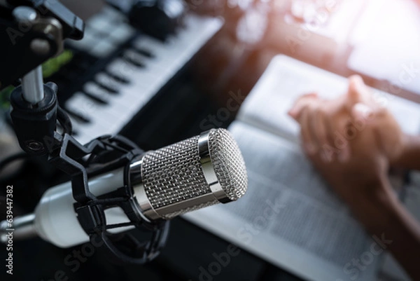 Fototapeta Microphone on desk with person praying, preacher reads the bible online, Christian podcast studio interior, records a podcast, online radio broadcast.