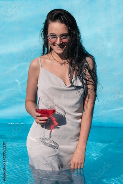 Obraz Beautiful girl with a glass of alcohol posing in the pool, summer vacation