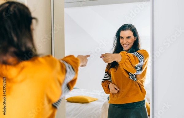 Fototapeta Self confident single woman pointing finger at reflection in mirror dancing and felling good. Independent person with high self esteem talk positive I can do it motivation.
