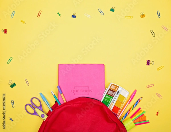 Obraz A red school backpack is lying on a yellow background and school supplies are sticking out of it. Back to school.