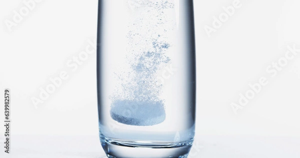 Fototapeta Tablets Falling and Dissolving into a Glass of Water against White Background