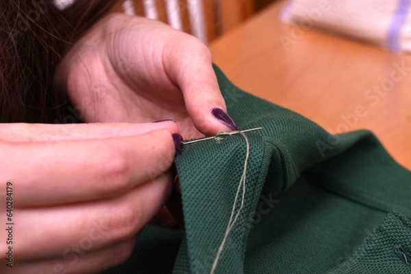 Obraz woman sewing with needle and thread a button on a green t-shirt