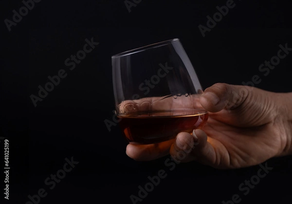 Fototapeta Hand holding glass of whiskey on black background