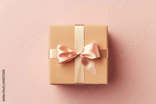 Fototapeta A gift box wrapped in cream paper and tied with a gold ribbon