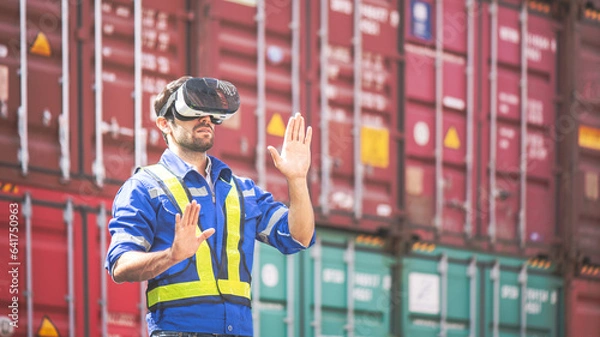 Fototapeta Engineer or technician wear VR (Virtual Reality) glasses and moves his hand like touching some icon in vr screen, with shipping freight cargo container dock in background. Logistic management concept.