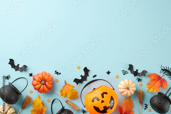 Fototapeta Immersing oneself in the ghostly atmosphere of Halloween. Top view photo of pumpkin basket, witch brooms, pots, pumpkins, autumn leaves, halloween decor on light blue background with promotional slot