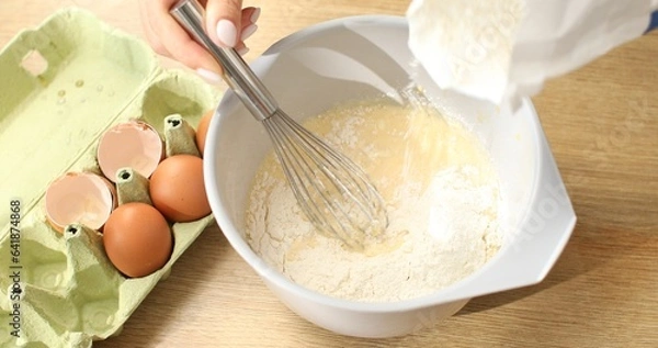 Fototapeta Flour is added to a bowl with beaten eggs. Making faffels or pancakes. Food preparation.