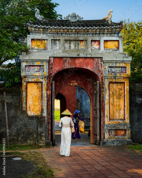 Fototapeta One of the colorful gates in the citadel of Hue. In the photo, two women standing backwards in the gate in traditional Vietnamese clothing. Vietnam.