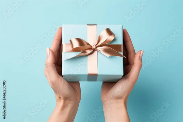 Fototapeta Feel the anticipation of receiving a gift as female hands hold a gift box against a light blue background, creating a sense of excitement and surprise. Generative AI.